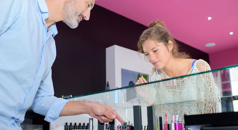 Woman looking into vape display cabinet with shop manager pointing towards a device.